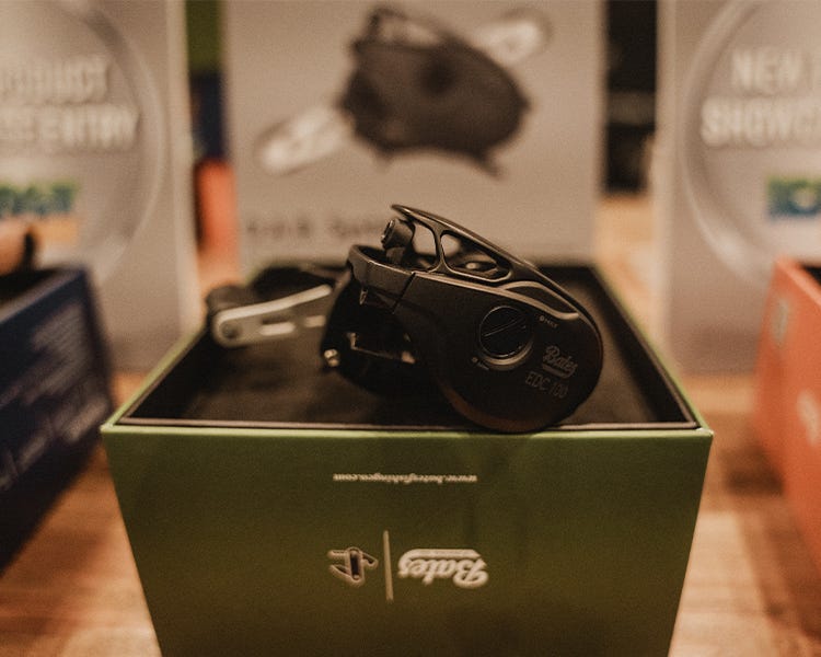 Bates EDC 100 baitcasting reel, highlighting its compact aluminum frame and digital braking dial, displayed under booth lighting. at ICAST 2025