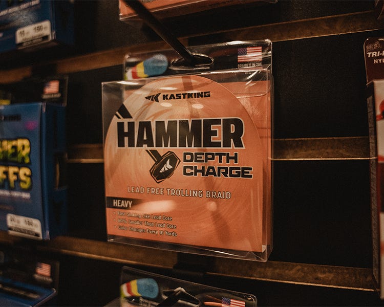 Spool of KastKing Hammer Depth Charge non-lead sinking line on a rock near water, emphasizing eco-friendly packaging and braid texture. Hanging on the wall at the kastking booth at the 2025 ICAST show.
