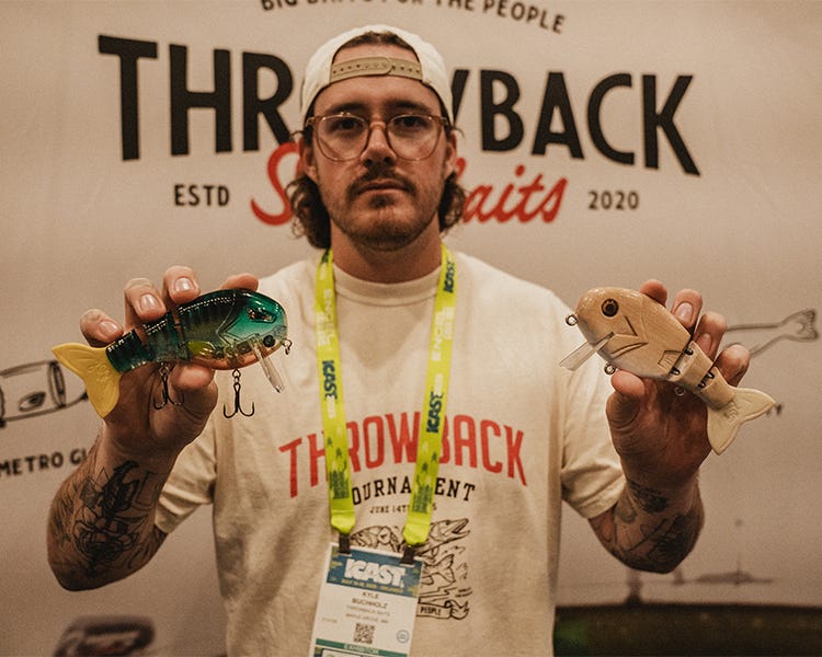 Holding two Throwback Swimbaits Wake Walker glidebait with retro paint job and jointed body, at the 2025 ICAST booth. 