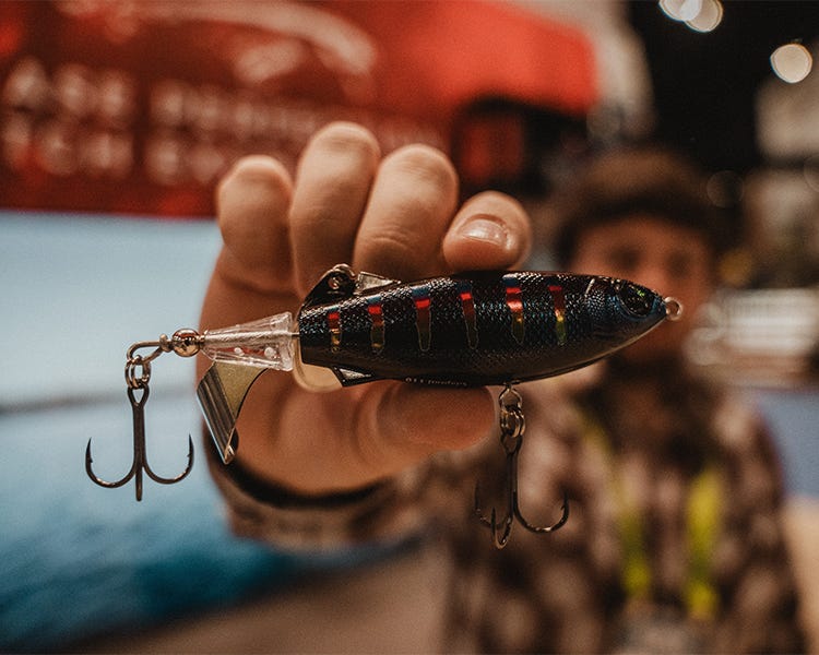 Rapala Claptail topwater bait with segmented tail design, mid-air shot showing surface splash effect and tail vibration mechanics at the Rapala booth at the 2025 ICAST show. 