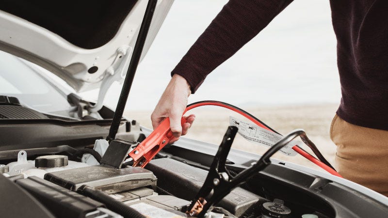 a man applies jumper cables to a car battery