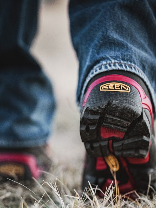 Red and black Keen boots at ground level walking away