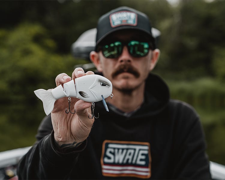 chris sitting on the deck of his boat, holding up the throwback baits wakewalker swimbait
