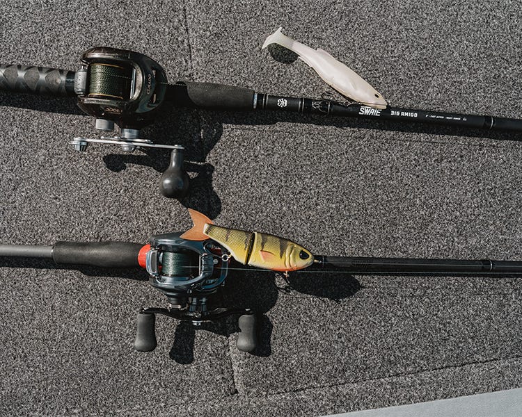 two swimbait combos laying on the deck, one the swate big amigo with a shimano curado reel, the other a swate brigade black label rod with a daiwa tatutla, with a throwback baits and a megabass magdraft tied on