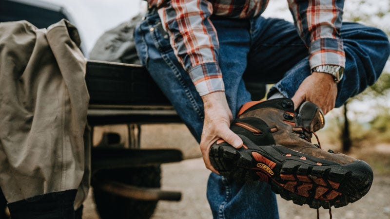 A man sits on a truck tailgate while putting on a pair of Keen hiking boots.