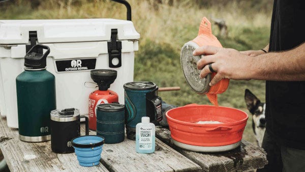 A camper making eggs in a pan next to an Outdoor Revival cooler and drink holder