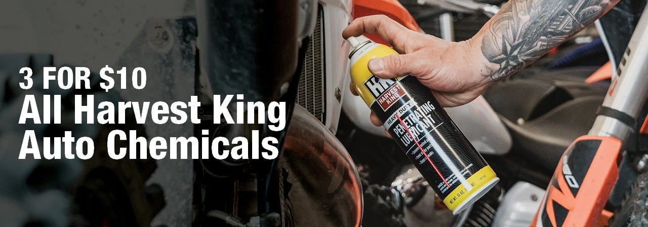 A tattooed person sprays a can of Harvest King heavy duty penetrating lubricant onto a motorcycle part, with large text stating "3 FOR $10 All Harvest King Auto Chemicals" on the left side.