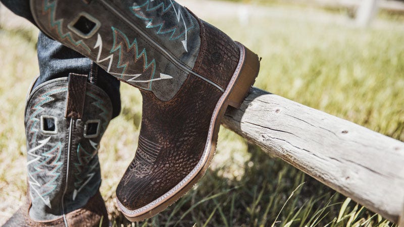 A pair of decorated square toe boots are work while leaned up against a fence post