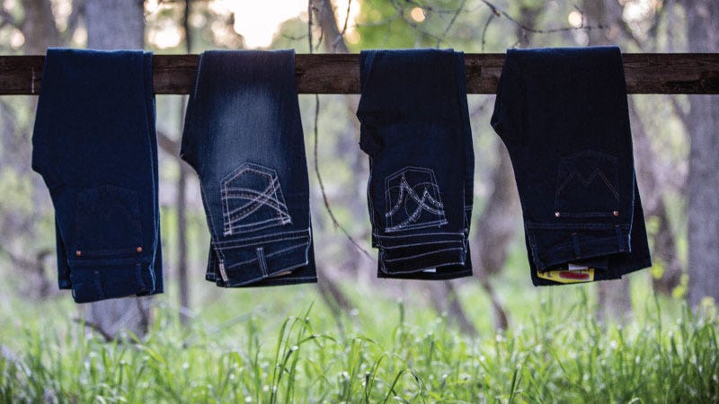 Four pairs of wrangler jeans hand holded over a wooden horizontal fence post